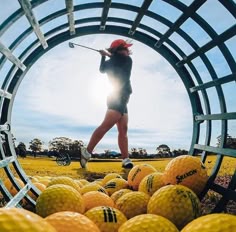 a woman is playing golf in a hole with many balls on the ground and another person behind her
