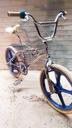 a bike that is sitting on the ground in front of a brick wall with blue spokes