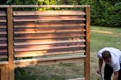 a man in white shirt and black pants working on a wooden structure with wood slats