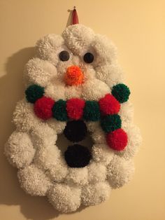 a snowman wreath hanging on the wall with pom - poms around it