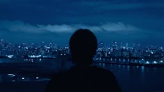 a person standing in front of a city skyline at night with the lights on and buildings lit up