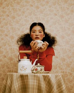 a woman sitting at a table with a tea pot