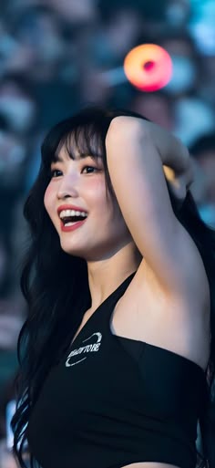 a woman with long black hair is smiling and holding her arm up in the air