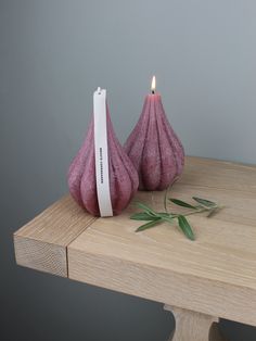two pink vases sitting on top of a wooden table next to a lit candle