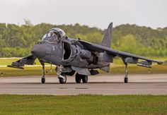 a fighter jet sitting on top of an airport tarmac with trees in the background