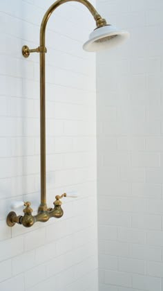 a shower head and faucet in a white tiled bathroom with gold fixtures on the wall