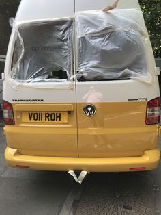 the back end of a yellow van with plastic covering it's windows and doors