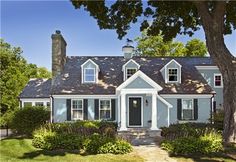 a gray house with white trim and yellow door in the middle of a green yard