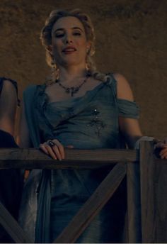 two women in dresses standing next to each other on a wooden fence with their hands on the railing