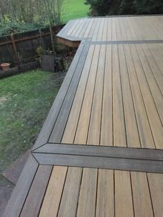 a large wooden deck in the middle of a yard with grass and trees behind it