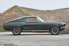 an old green mustang sitting on top of a dirt road