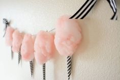 pink pom - poms are hanging on the wall next to black and white striped ribbon