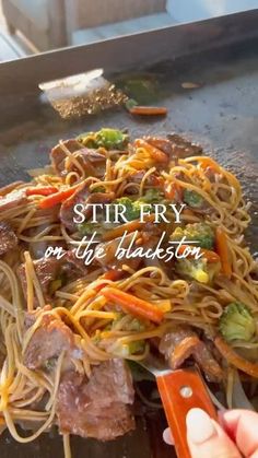 stir fry on the table with noodles and vegetables being cut by someone holding a knife