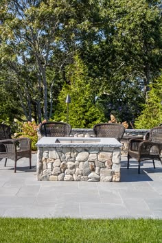 an outdoor fire pit surrounded by wicker chairs and tables with trees in the background