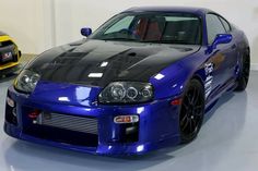 two cars parked side by side in a garage, one is blue and the other is yellow
