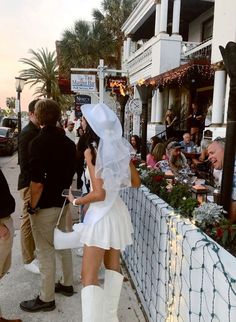 a woman dressed in white is standing by a fence with people looking at the camera