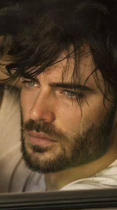 a man with long hair and blue eyes looking out the window at another man wearing a white t - shirt