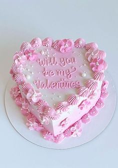 a heart - shaped cake with pink frosting and flowers on the side that says, will you be my valentine?