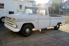 an old white pickup truck parked in front of a trailer
