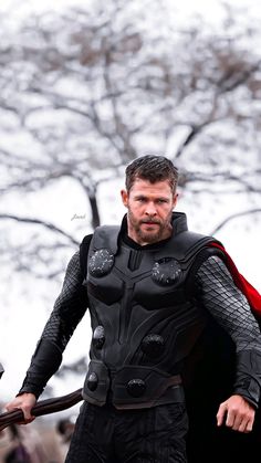 a man dressed as thor stands in front of a tree with his hands on his hips