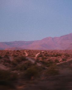 an airplane is flying in the sky over some hills and scrub trees with mountains in the background