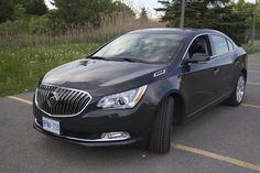 a black car parked in a parking lot next to some grass and trees on the side of the road