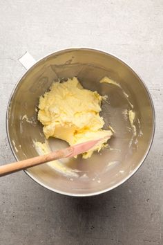 a metal bowl filled with yellow batter and a wooden spatula on top of it