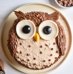 an owl cake with chocolate frosting and googly eyes on a plate next to bowls of cereal