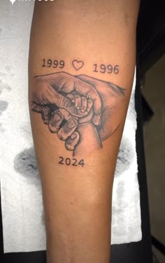 a tattoo on the arm of a person holding a baby's hand with two hands