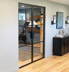 an empty room with glass doors leading to the gym area and exercise equipment in the background