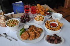 a table topped with plates of food and bowls filled with different types of foods next to glasses of wine