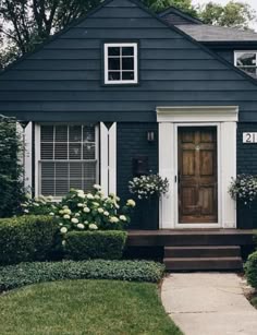 a black house with white shutters and flowers on the front door is seen in this image