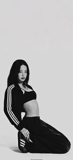 a woman is sitting on the ground wearing black pants and a cropped top with white stripes