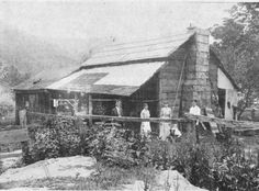 an old black and white photo of people standing on the porch of a log cabin