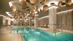a large indoor swimming pool with lots of lights hanging from the ceiling and chairs around it