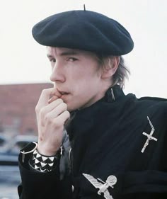 a young man wearing a black hat with crosses on it and holding his finger to his mouth