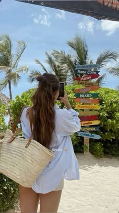 a woman is walking on the beach with a straw bag and cell phone in her hand