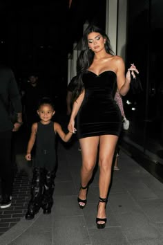 a woman in a short black dress holding hands with a small child