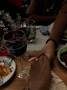 two people sitting at a table with plates of food and glasses of wine in front of them