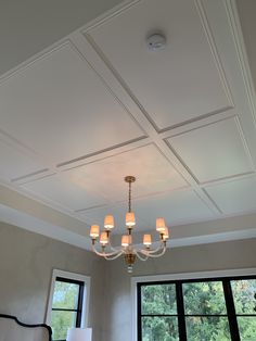 a chandelier hanging from the ceiling in a room with large windows and two lamps