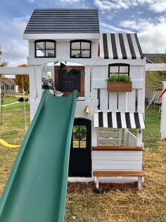 a play house with a slide in the front and windows on the back, next to a grassy area