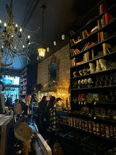 people are standing in a store with many items on shelves and lights hanging from the ceiling