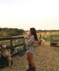 a woman holding a baby in her arms while standing next to some goats and sheep