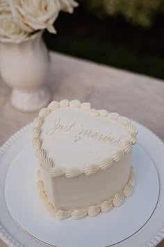 a heart shaped cake sitting on top of a white plate next to a vase with flowers