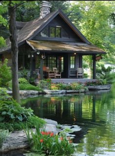 a small house sitting on top of a lush green hillside next to a lake with lily pads