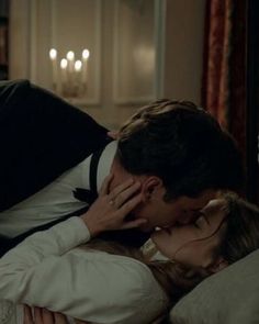 a man kissing a woman on the cheek while laying in bed with candles behind him
