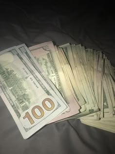 a pile of money sitting on top of a bed next to another pile of hundred dollar bills