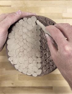 two hands are holding a plate with white circles on it, and one hand is using a pencil to draw something