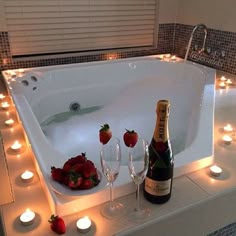 a bottle of champagne and some strawberries in a bathtub with candles around it