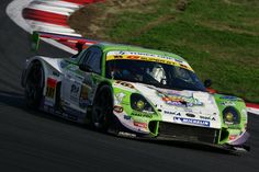 a green and white race car driving on a track with grass in the back ground